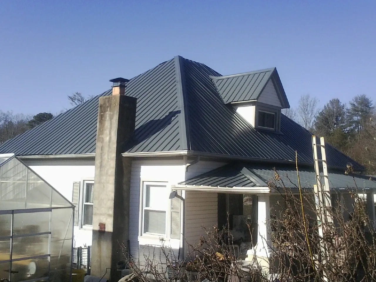 Dark blue standing seam metal roof on a white farmhouse with dormer — Slate & Tile Roof Repair by Roofing Brothers in Gonvick