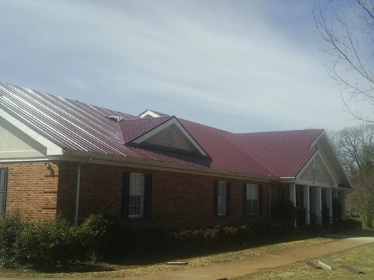Red metal roof with gabled entries on a long brick building, from a Hail Damage Roof Repair job in Gonvick