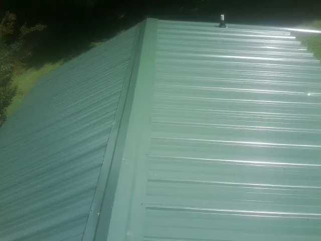 New green metal panels meeting at the ridge of a roof — Flat Roof Repair work by our crew in Gonvick