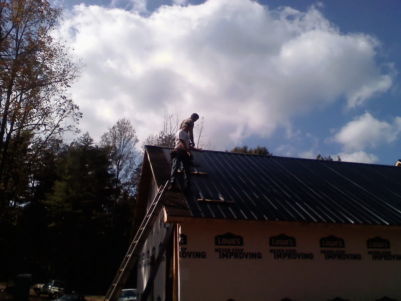 Roofer fastening dark metal panels high against a cloudy sky, from a Roof Inspection job in Gonvick